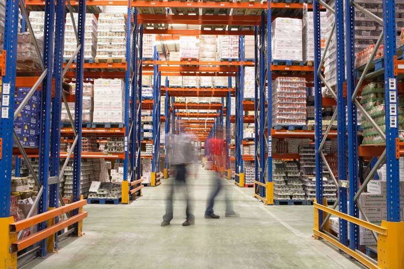 Warehouse interior with two blurred workers, symbolizing the decisions needed to be made to choose the right warehouse management system.